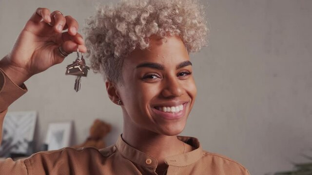 Close up focus on keys in hands of blurred smiling young african american female. Happy millennial multiracial woman homeowner feeling excited of purchasing first own apartment accommodation or house