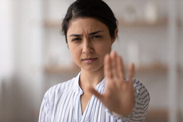 Portrait of unhappy distressed young Indian woman show stop no hand gesture sign against domestic...