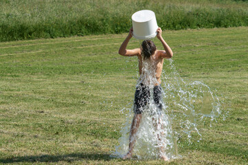 Teenage boy pouring bucket of cold water over his head outdoors. Ice water challenge. Cold water therapy benefits - obrazy, fototapety, plakaty