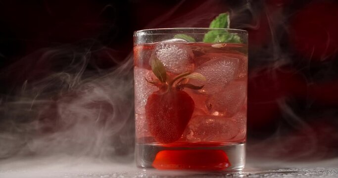 Cold glass with red cocktail is spinning slowly in the smoke on the dark background, alcohol drinks and beverage, non-alcohol cocktail, object video of lemonade, 4k Prores HQ