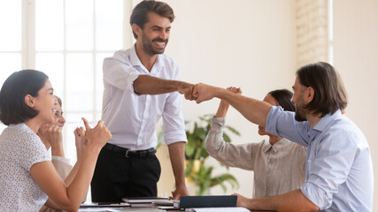 Smiling confident executive fists bumping with employee at corporate meeting, colleagues cheering, team leader thanking worker for good work result, celebrating success, business achievement