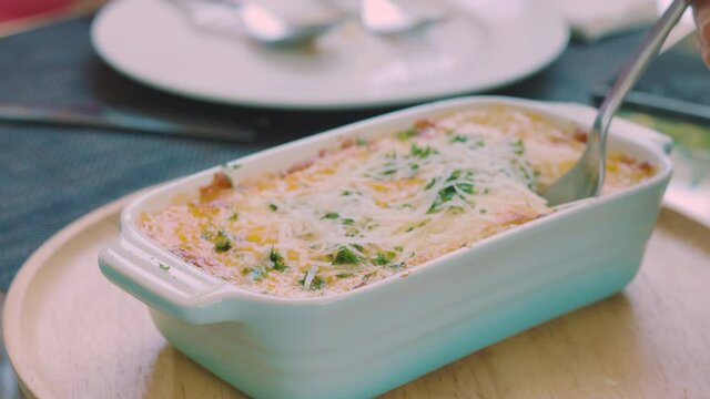 Close up 4k of lasagne or grating prepared by baking ingredient food with vegetable and melted cheese looks delicious. Metal spoon is putting stretched cheese for meal in restaurant.
