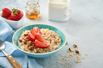 Oatmeal porridge with strawberry slices, nuts almonds and honey in blue bowl on grey table. Healthy eating, dieting, vegetarian food concept. Place for text