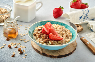 Oatmeal porridge with strawberry slices, nuts almonds and honey in blue bowl on grey table. Healthy eating, dieting, vegetarian food concept. Place for text
