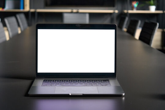 Workplace In Conference Room With Laptop Pc Computer On Desk With Blank Empty Mockup Screen For Advertising Standing In Dark Modern Contemporary Office. No People. Business Technologies Concept.