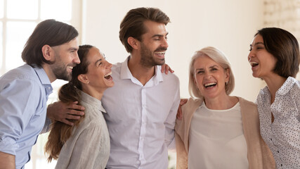 Excited multiethnic business people laughing and embracing, celebrating shared corporate success or...