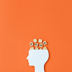 Silhouette of human head and wooden blocks with the lettering ADHD on orange background. Concept of attention deficit hyperactivity disorder. Place for text - obrazy, fototapety, plakaty