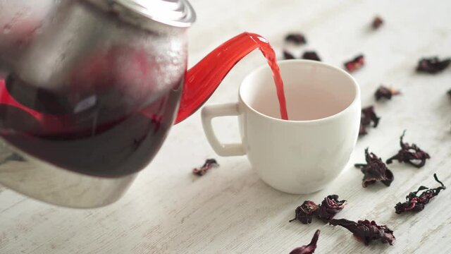 Red drink is poured from glass teapot. Freshly brewed tea with raspberries, tea with viburnum, tea with hibiscus, tea from tea rose petals. Health and homeopathy concept. Red tea is poured into cup on