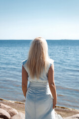 Fototapeta na wymiar Young beautiful blonde hair woman in blue jeans dress looking at the sea