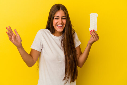 Young caucasian woman holding a compress isolated on yellow background receiving a pleasant surprise, excited and raising hands.