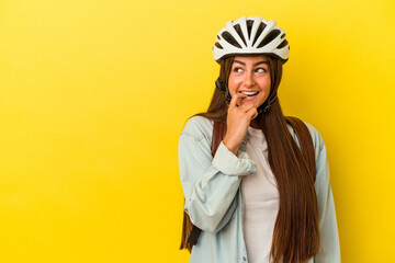 Young student caucasian woman wearing a bike helmet isolated on yellow background relaxed thinking about something looking at a copy space.