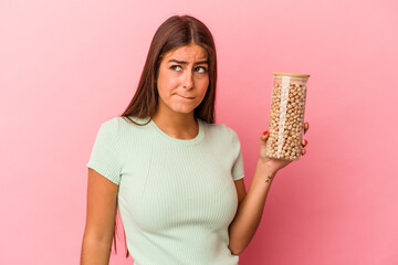 Young caucasian woman holding a chickpeas jar isolated on pink background confused, feels doubtful...