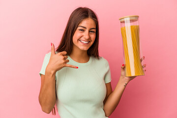 Young caucasian woman holding a pasta jar isolated on pink background showing a mobile phone call gesture with fingers.