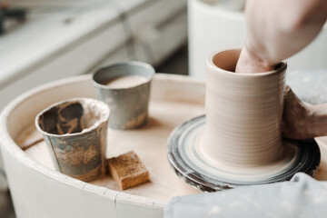 Photo near and side. The girl's hands are making a clay vase on a potter's wheel. Clay dishes
