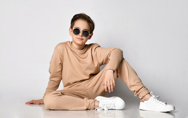 Cool teenage boy in casual sportswear and trendy sunglasses feels happy sitting against the...