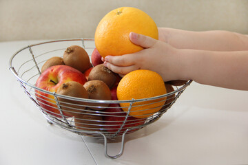 A bowl of fruit. The child takes fruit from a vase and different fruits