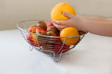 A bowl of fruit. The child takes fruit from a vase and different fruits