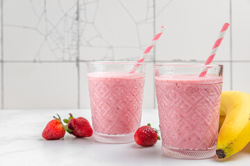 Strawberry and banana smoothie or milkshake in glasses with fresh fruits and berries on white background