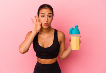 Young Venezuelan woman drinking a protein shake isolated on pink background trying to listening a gossip.