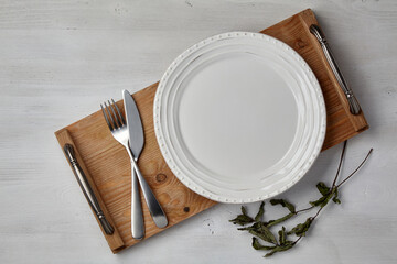 A white ceramic plate and a tray of cutlery on a light painted wooden table