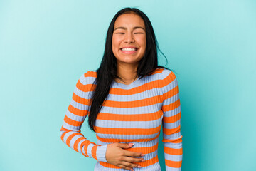 Young Venezuelan woman isolated on blue background touches tummy, smiles gently, eating and satisfaction concept.