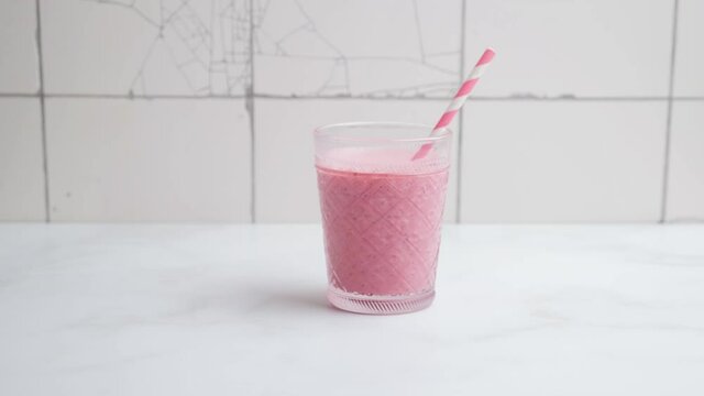 Man puts on white table two glasses of pink strawberry milkshake or smoothie with the straws. 4k video. Healthy summer drinks