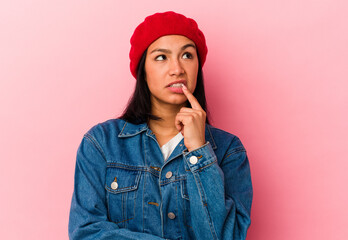 Young Venezuelan woman isolated on pink background looking sideways with doubtful and skeptical expression.