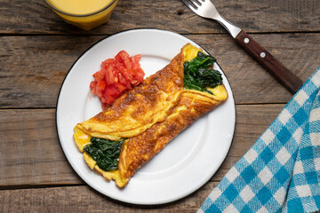 Egg omelette with spinach and tomate on wooden background. French food