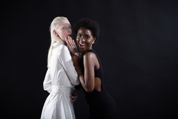 Caucasian albino girl and african american young woman hugging on black background. Women friendship, lgbt love and relationships concept.