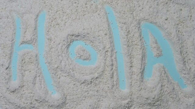 Hello in Spanish. The word Hola is drawn in the sand
