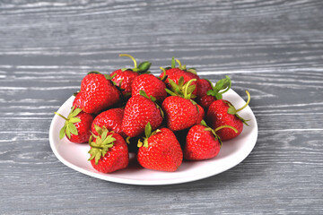 red large strawberries in a white plate on a natural grey  background close-up, selective focus