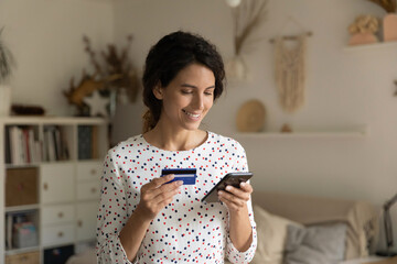 Smiling woman paying online by credit card, using smartphone, happy attractive young female...
