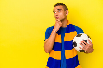 Young venezuelan man watching soccer isolated on yellow background looking sideways with doubtful and skeptical expression. - obrazy, fototapety, plakaty