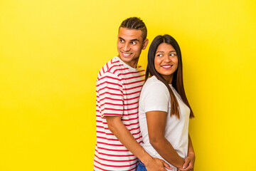 Young latin couple isolated on yellow background looks aside smiling, cheerful and pleasant.