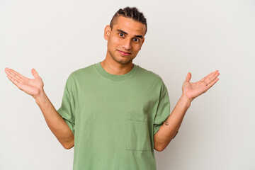 Young venezuelan man isolated on white background confused and doubtful shrugging shoulders to hold...