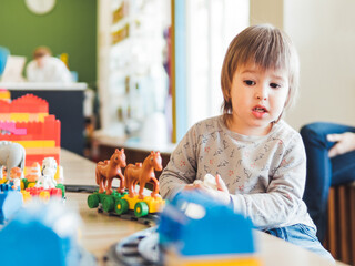 Toddler plays with colorful toy blocks. Little boy stares on figure from toy constructor. Interior of kindergarten or nursery. Indoors leisure activity for children.