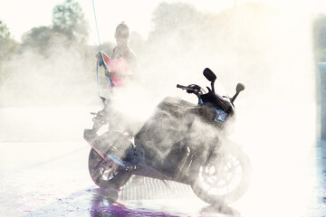 Beautiful stunning girl washes a motorcycle in self service carwash with high pressure water jet in...