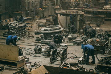 Large workshop with metallurgical plant workers working with cast iron parts, post-casting...