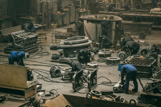 Large workshop with metallurgical plant workers working with cast iron parts, post-casting processing at steel mill foundry.