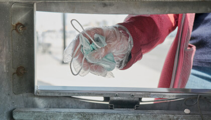 Woman wearing gloves throws protective medical mask against the virus into the trash. The concept of lifting lockdown restrictions and ending the virus pandemic. The camera shoots out of the basket