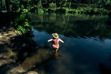 A woman standing on her waist-deep in the water of a forest river in a mountainous area.