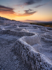 Summer landscape during sunset. The view of the travertines and the bright sunset. Calcium terraces without water. A popular place for tourism. White rocks and sunset. Pamukale, Turkey.