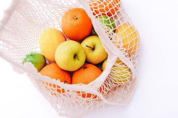 Cotton mesh bag with fresh colorful fruits on light background, close up. Zero waste concept
