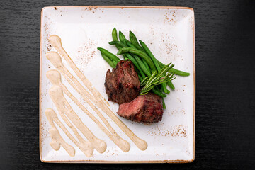 Filet mignon with asparagus on a light plate, on a dark background