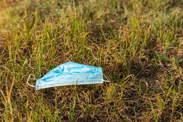 Thrown away or lost mouth masks on the ground in grass, outdoor,A used, blue surgical mask used for COVID-19 PPE protection.