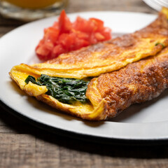 Egg omelette with spinach and tomate on wooden background. French food
