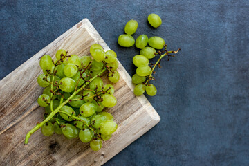 Green grapes on rustic wooden cutting board on dark slate background.
