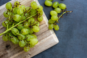 Green grapes on rustic wooden cutting board on dark slate background.