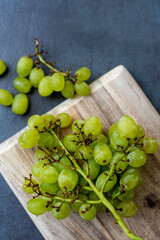 Green grapes on rustic wooden cutting board on dark slate background.