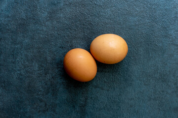 Two brown eggs on textured dark gray slate background.